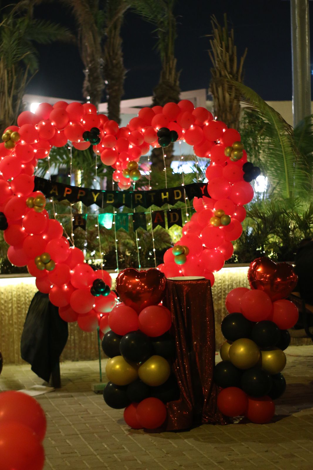 Outdoor birthday surprise decoration Karachi with red heart balloon arch and red black gold balloon pillars – image 1