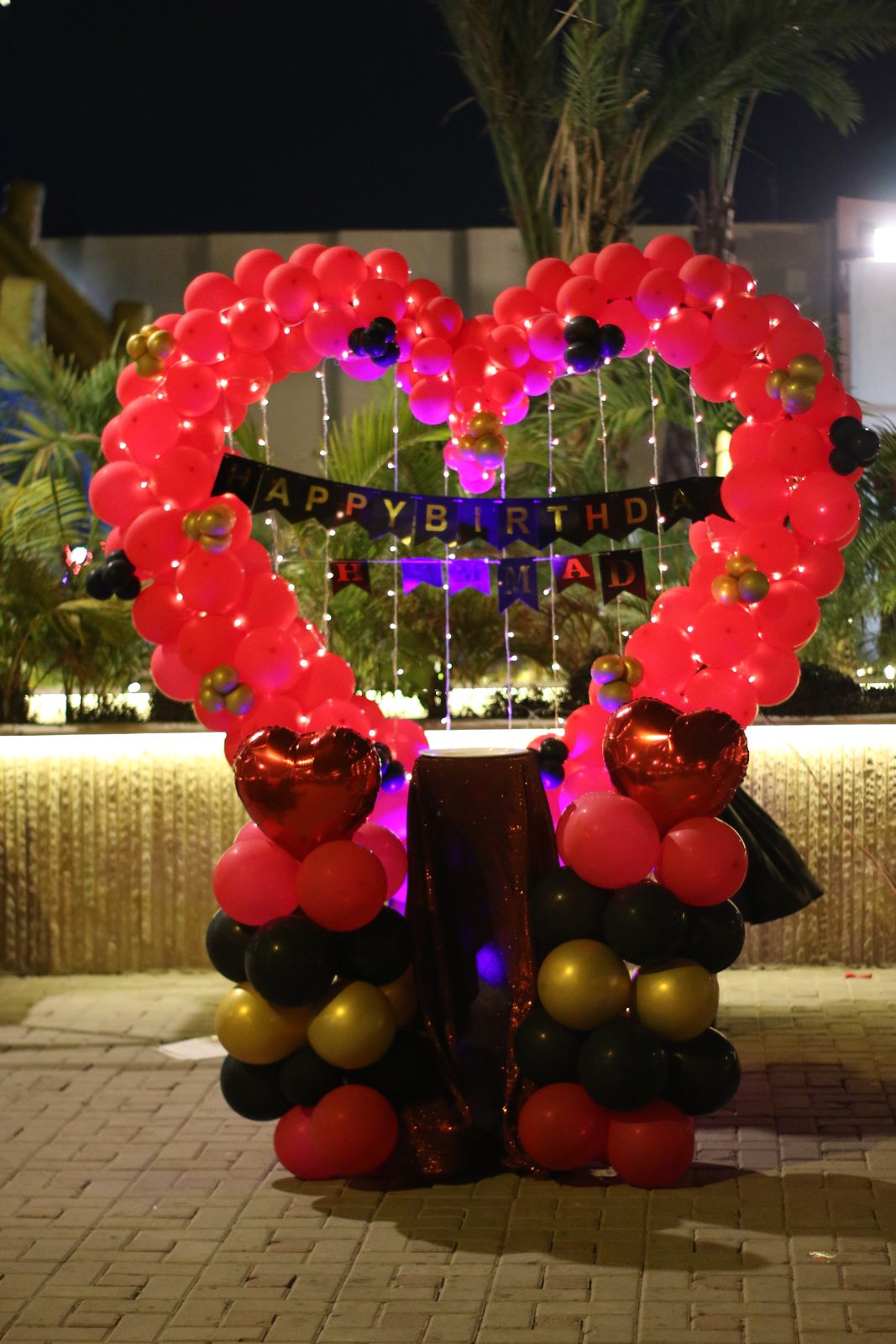Outdoor birthday surprise decoration Karachi with red heart balloon arch and red black gold balloon pillars – image 2