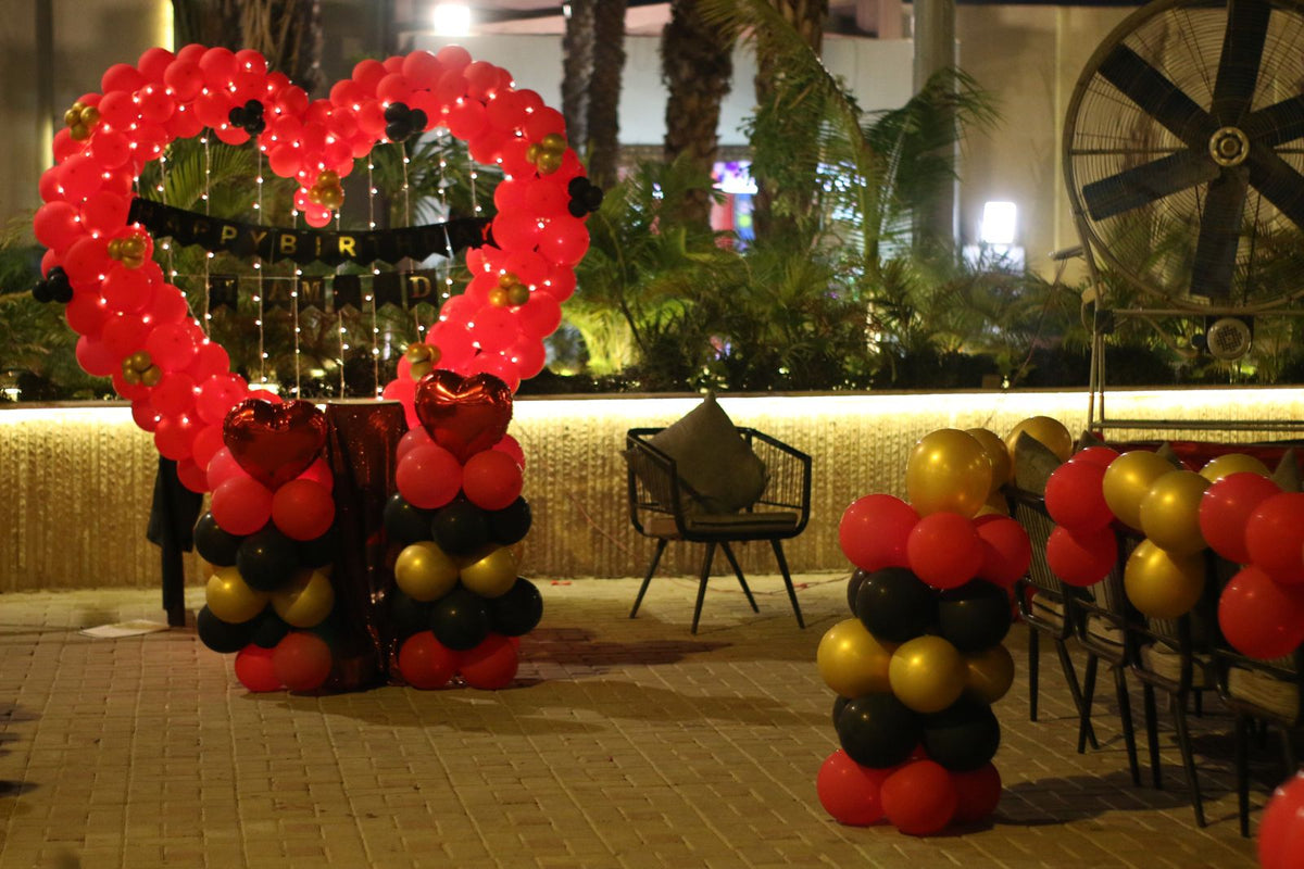 Outdoor birthday surprise decoration Karachi with red heart balloon arch and red black gold balloon pillars – image 3