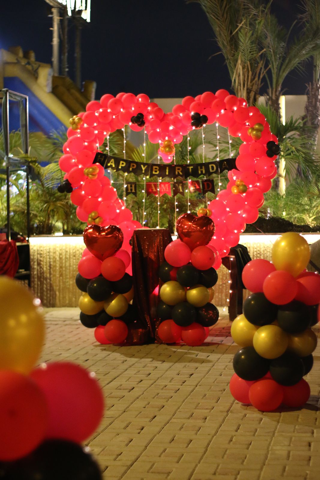 Outdoor birthday surprise decoration Karachi with red heart balloon arch and red black gold balloon pillars – image 4